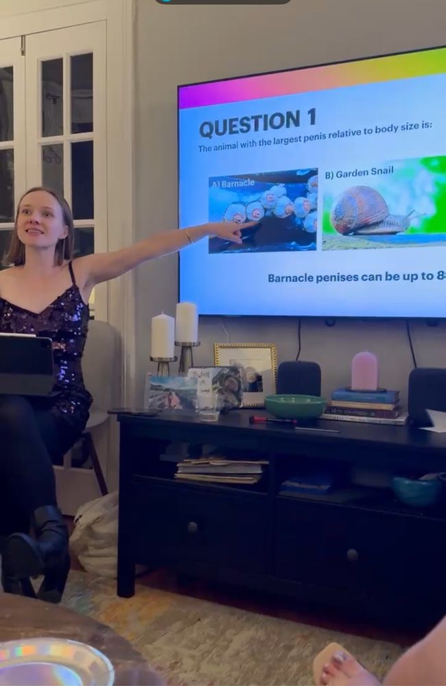 Me, dressed in purple sequins, pointing to slide show on a tv in which the slide is discussing barnacle.