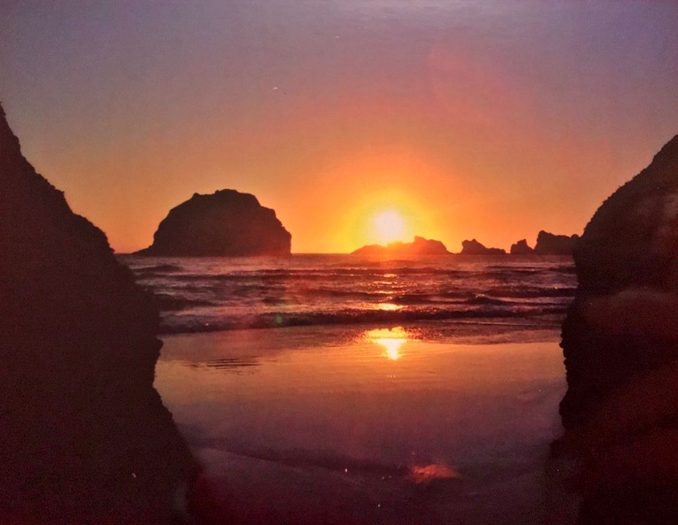 The sun sets behind a face-shaped rock and other seastacks on the Pacific coast.