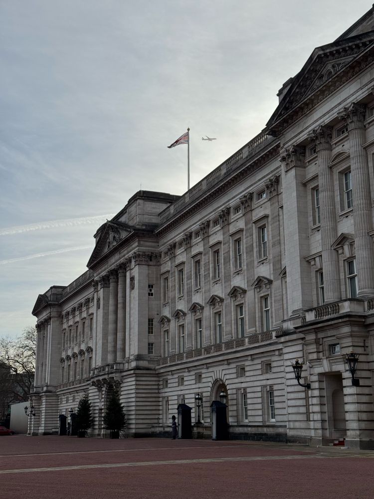 Palas Buckingham, heb y brenin, ond gyda rhai gwarchodwyr ac awyren uwchben. Buckingham Palace, without the king, but with some guards and an aeroplane overhead. 