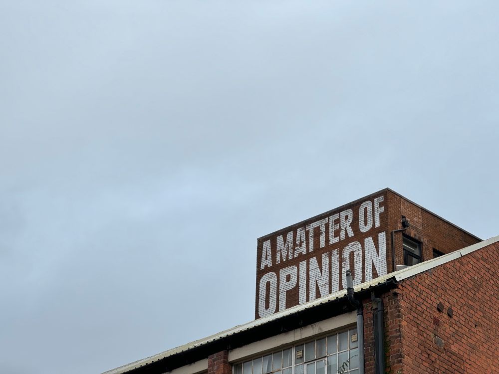 A derelict factory with painted text on a brick wall: “A matter of opinion”. "Mater o farn" wedi'i baentio mewn gwyn ar wal frics ffatri segur
