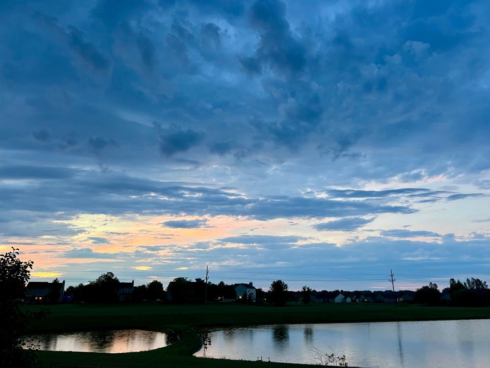 Cornflower blue clouds over yellow and peach, pond reflecting the same colors