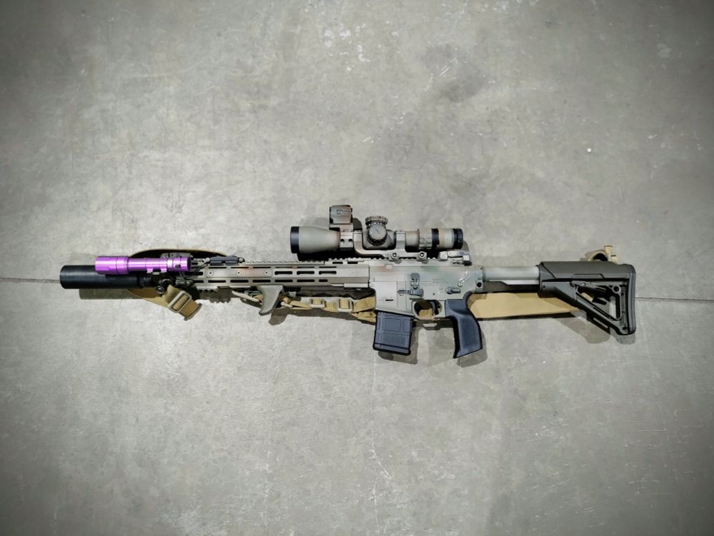 a sixteen inch camouflage spray painted suppressed aye are fifteen with a two point five to ten ex medium power variable optic and an inline mounted red dot sight