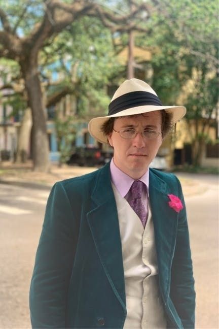 a sour looking little man dressed like an oompa loompa cosplaying as a slave trader in a blaxploitation flick