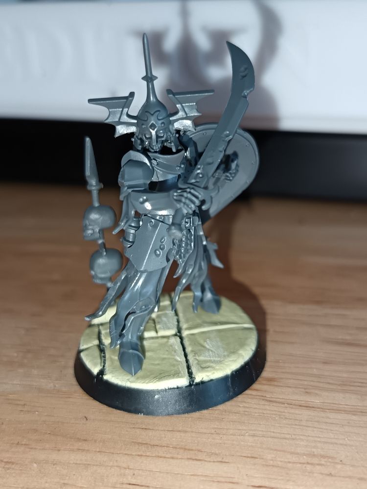 The Warhammer free mini of the month, a skeleton in armour with a sword and shield, stands on the custom base with it's back to the standing pike.