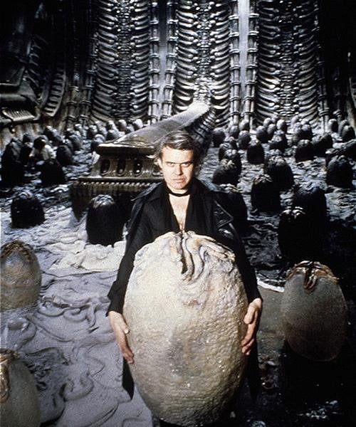 HR Giger posing with a giant egg on the set of Alien, looking intensely at the camera 