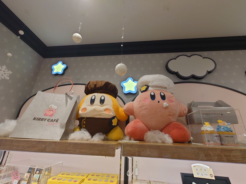 天王寺MIOのカービィカフェの写真
右側にカービィ。白いパティシエ帽をかぶって、口元にクリームを付けている。
左側にワドルディ。こげ茶のカフェエプロンと帽子を身に着けている。
