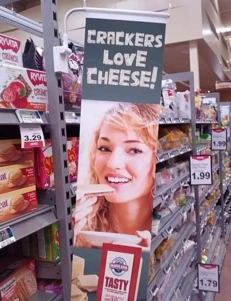 A grocery store aisle with a tall picture of a blond haired whit woman eating a cracker. Above the picture are the words “crackers love cheese”. 