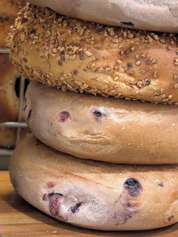 The side of a blueberry bagel in a stack of several. The eyes are little blueberries, and the mouth is a fold in the bread. The lips look like a little kid pouting.