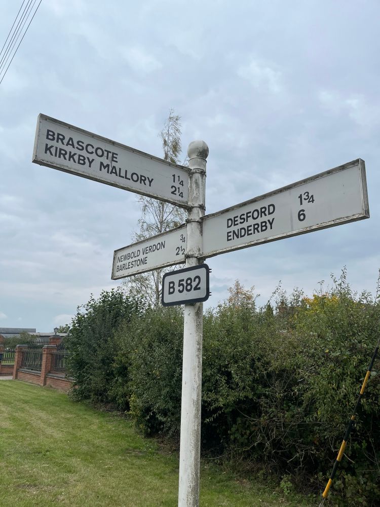 A white three-way signpost with black lettering on the B582 east of Newbold Verdon in Leicestershire. It has directions to Brascote, Kirkby Mallory, Desford, Enderby, Newbold Verdon and Barlestone.