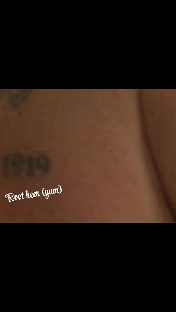 A closeup of Platner's skin where he has a 1919 tattoo. 
Edited below that is some swoopy text that says "Root beer (yum)"