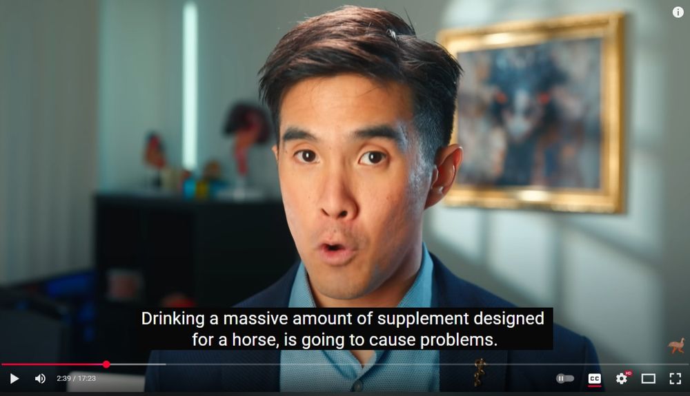 Some dude is looking into the camera speaking. Wearing a suit with a lapel with the medical snake and staff on it. Behind him is a blurred background with a painting and a desk with knick knacks. Player interface for YouTube and the caption "Drinking a massive amount of supplement designed for a horse, is going to cause problems."