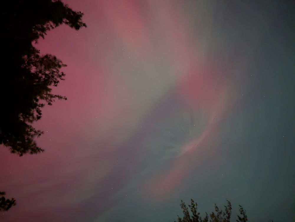 A picture of the night sky. There's a red and green aurora present that seems to originate from a single point, spreading out and forming an apparent eye in the sky.