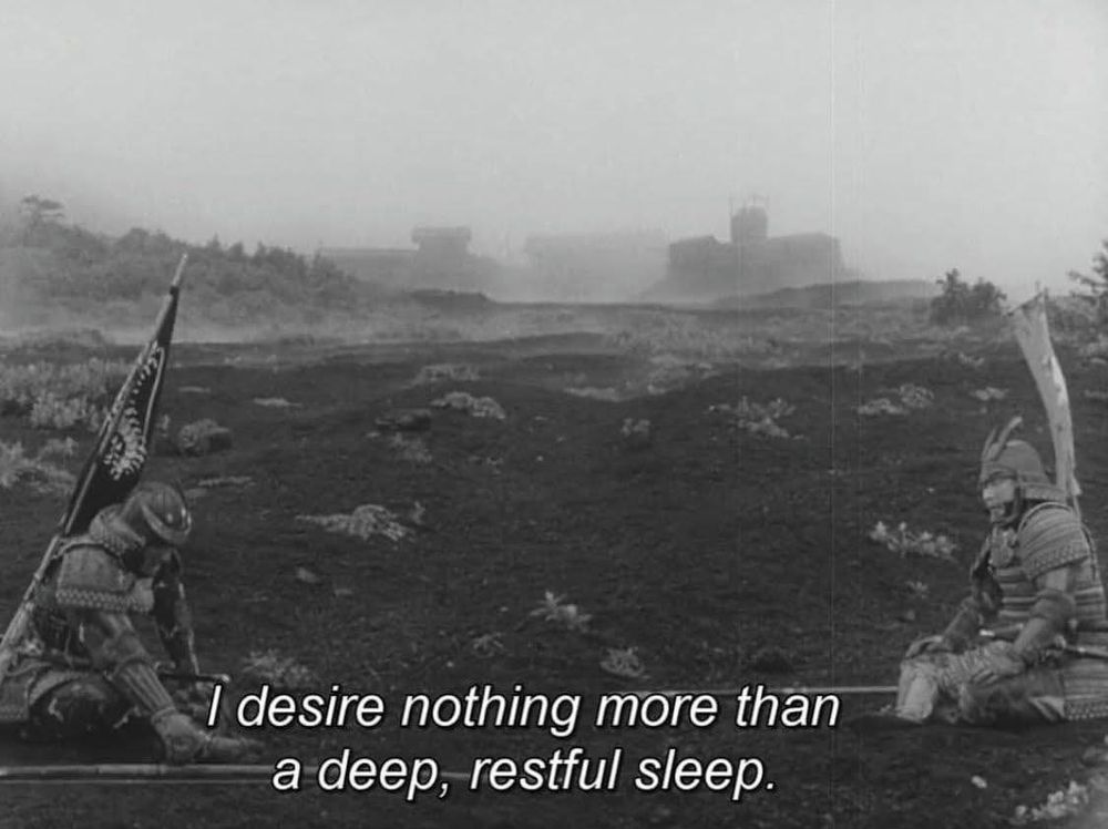 A black and white image of two samurai sitting a considerable distance from each other. They both have flags on their backs and weapons laid on the ground. There is a fog obscuring castles in the background, with a few shrubs being the only vegetation in the otherwise barren ground. A subtitle reads "I desire nothing more than a deep, restful sleep."