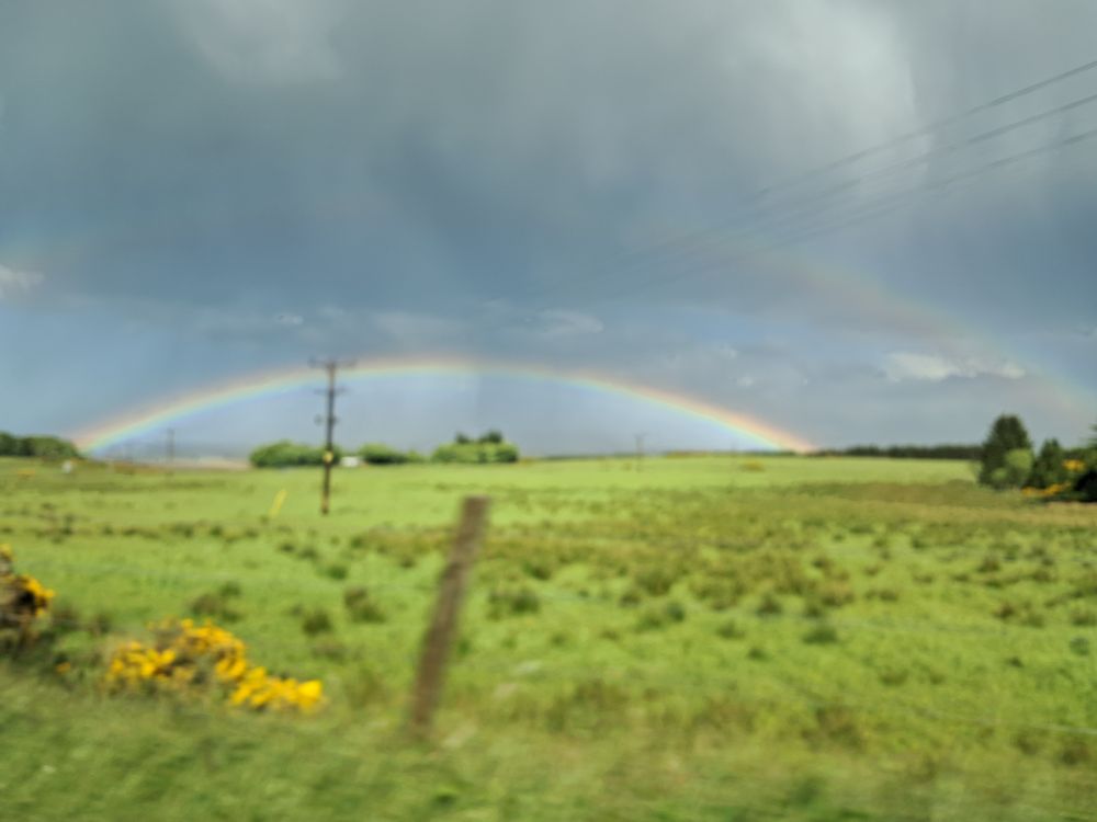 A low arc rainbow against a rain cloud sky with Spring green field and yellow gorse flowers. Could be anywhere in Scotland, I don't remember taking it. No I dont think I'd been drinking