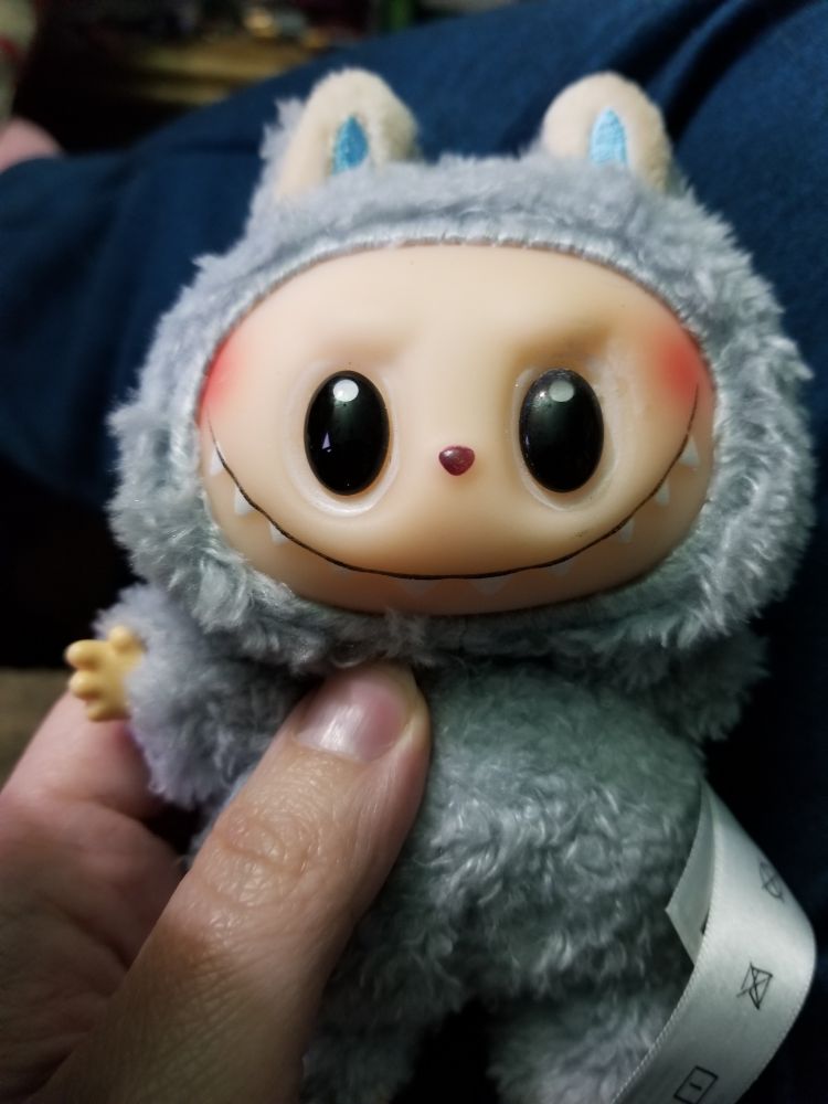 A fake dusty-blue Labubu keepchain held in someone's hand. It had glued on plastic eyes and an overly large smile