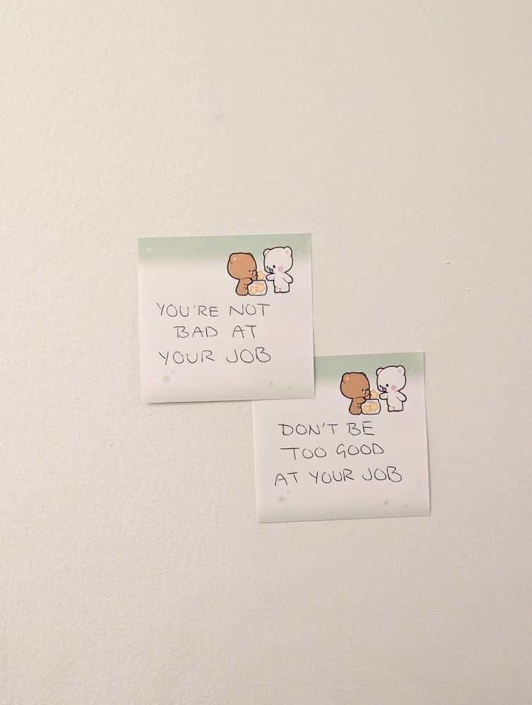 Two sticky notes stuck to a plain white wall. The first note says "you're not bad at your job". The second note is by the bottom right corner of the first note, and it says "don't be too good at your job".