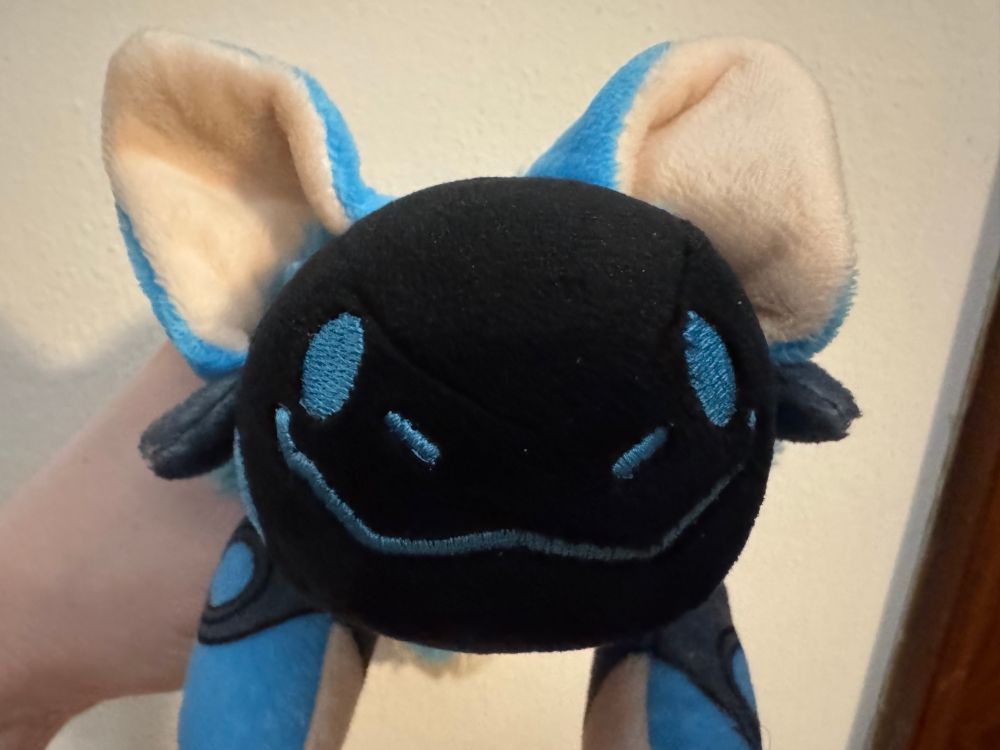 A blue Protogen Protobean looking at the viewer. It is being held by someone's hand.