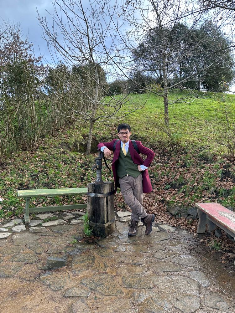 Derek in Bilbo Baggins cosplay poses by a water pump in the Hobbiton Movie Set.