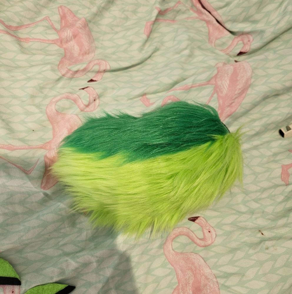 A photo of the fursuit tail, a short nub style tail, primarily lime green with a darker green top