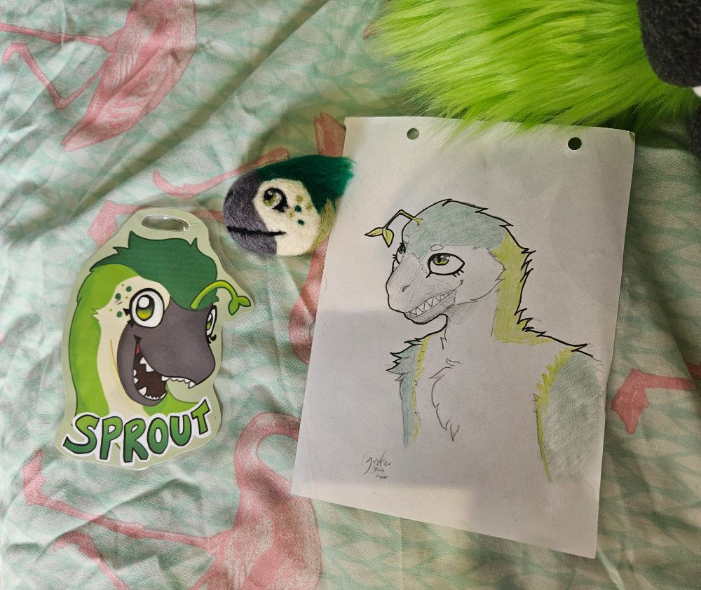 A close up of the art that comes with the fursuit - a laminated badge with the name "Sprout" on, a pencil drawing, and a needle-felted brooch