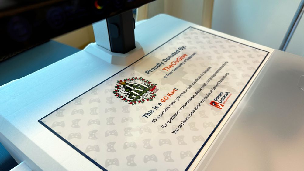 Close-up of a sign on a sleek, white surface, showcasing a colorful logo reading "Civ Give 2024". The text explains this is a "GO Kart," a portable video game kiosk donated by "The CivGive" and "their community of supporters" The sign features a background pattern of faint game controllers.