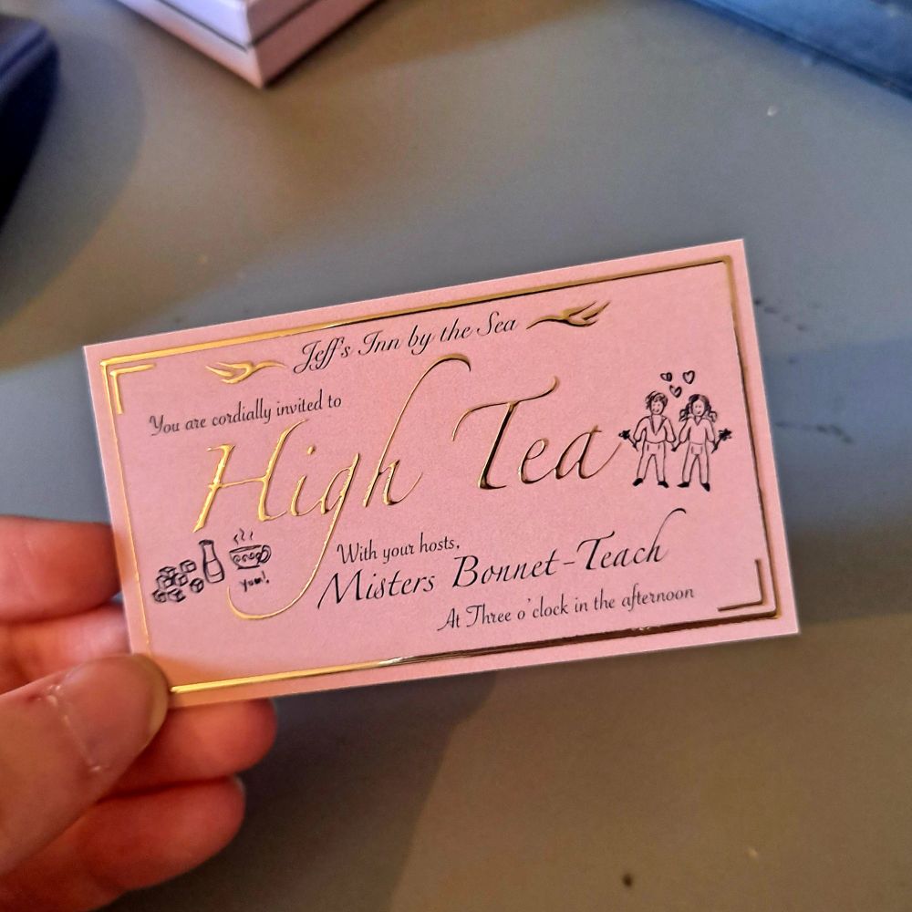 Photo of a hand holding an Invitation to High Tea with Misters Bonnet-Teach. The invite is pink with embossed gold lettering