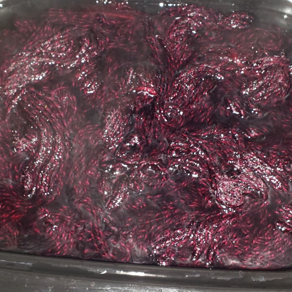 Close up shot of black and magenta colored yarn in dyepot.