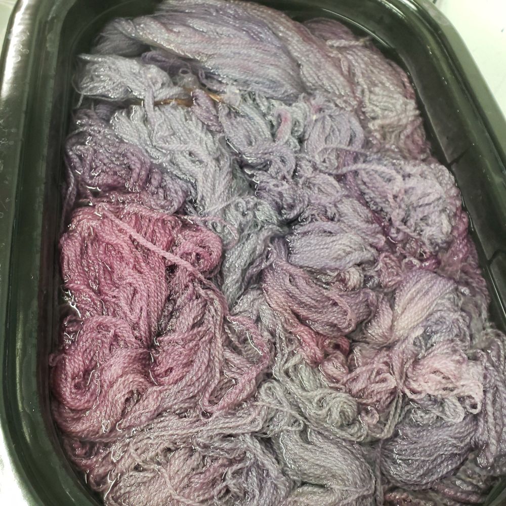 Yarn sits in large container, water visible, colors are a very pale lilac to a pale magenta