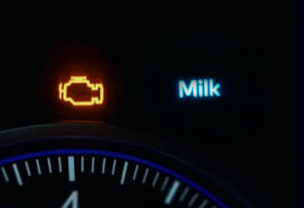 photo of a car dashboard above the speedometer with an orange engine light and a blue "milk" light