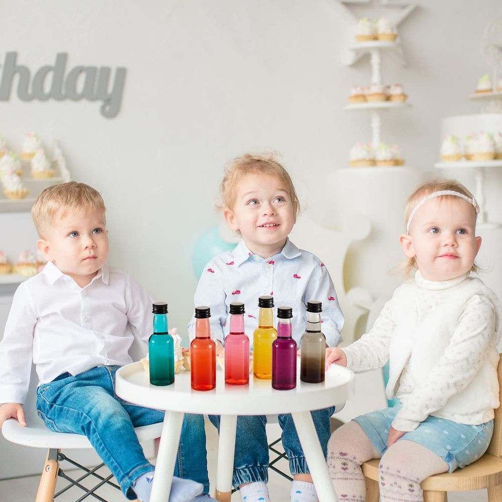 three toddlers sitting at a table with unlabeled colored bottles that look vaguely like liquor