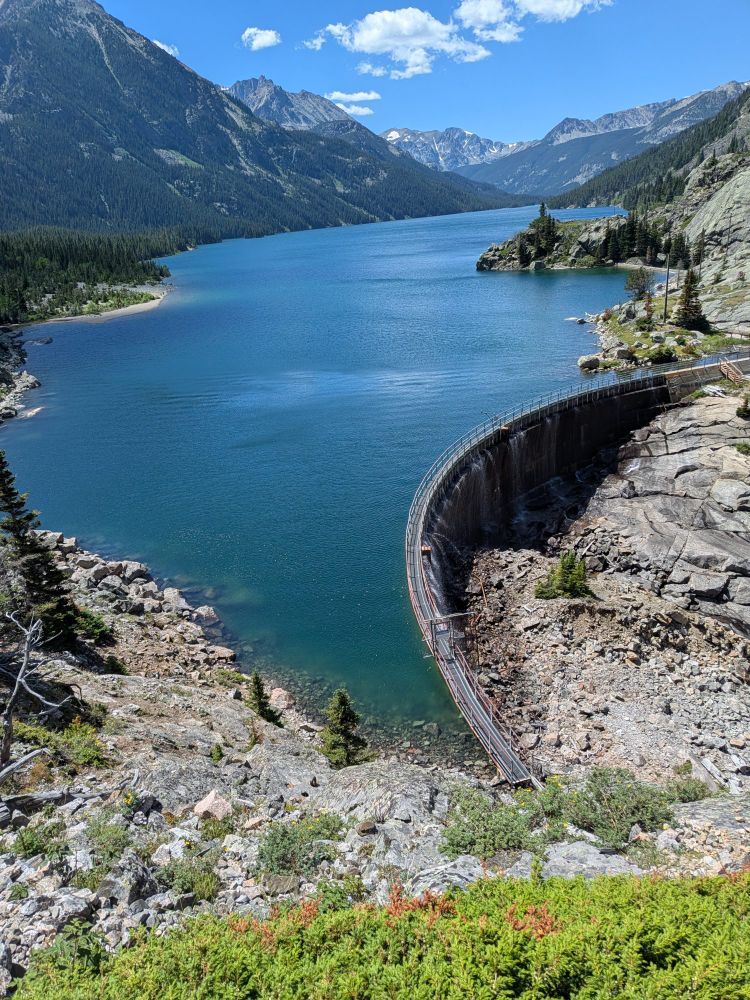 The clear blue water of Mystic lake in Montana, with mystic lake dam visible in the foreground.