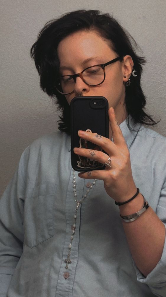 A mirror selfie of Moth. They are wearing a pastel blue button up shirt with long sleeves, the phone covering the bottom half of their face