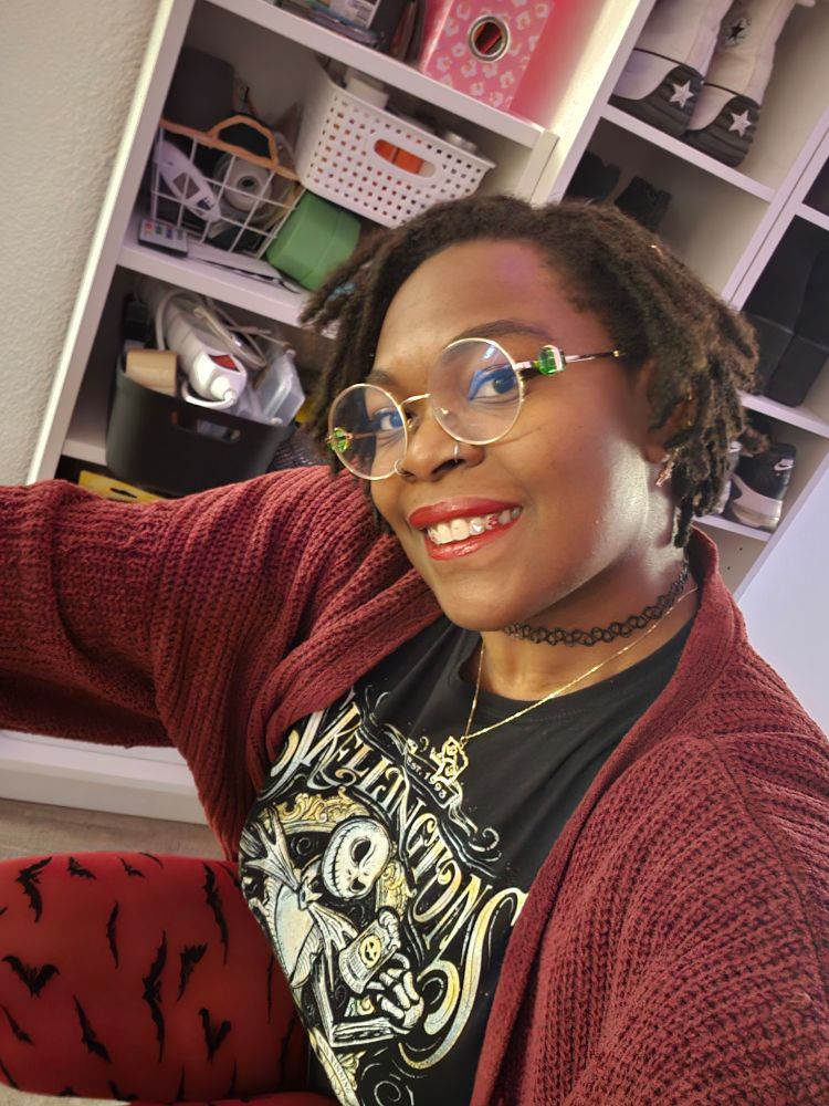 A picture of me with red clothe and a nightmare before Christmas black t shirt. I'm crouching and smiling at the camera. 