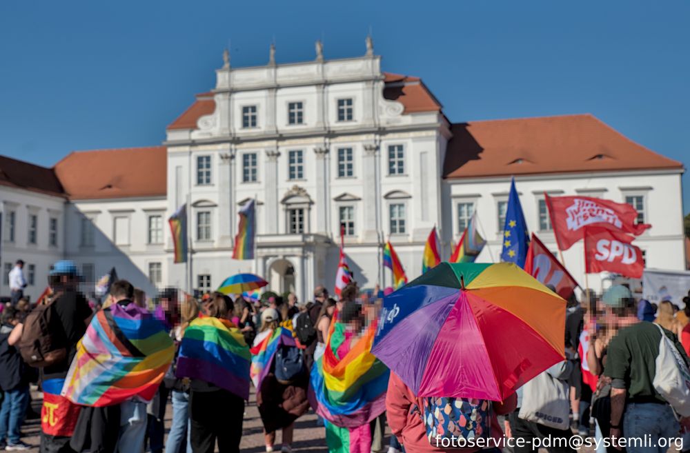 csd demo am endpunkt vor dem oranienburger schloss. im vordergrund eine person mit regenbogen-regenschirm und viele pridflags
