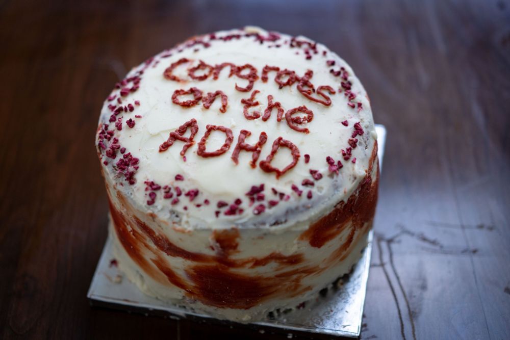 A round cake with white and red icing. On top it reads "Congrats on the ADHD" in red icing. 