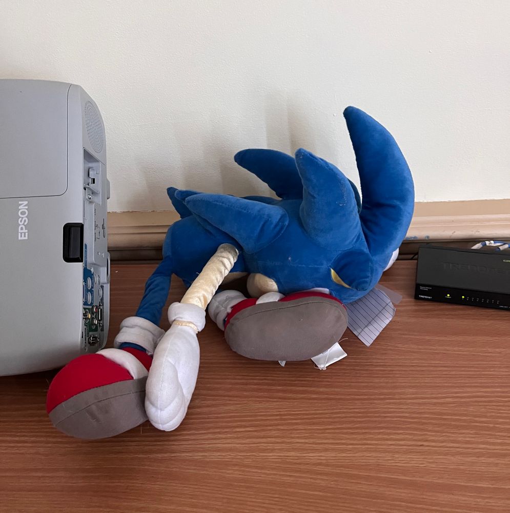 A sonic the hedgehog plush sitting on a table, crumpled, looking sad