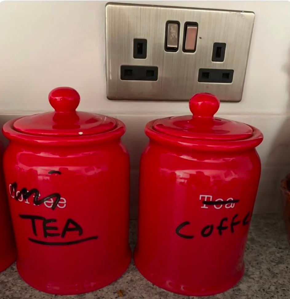 Two red ceramic jars, one with white text that says "coffee", the other says "tea". However, someone crossed these out with black sharpie and wrote the opposite word on each.