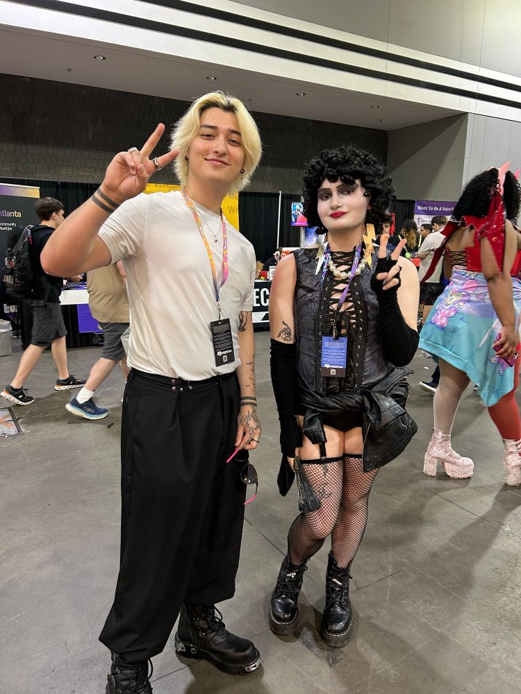 Danny Phantom.exe and a Frank n Furter cosplayer standing next to each other and doing peace signs at a convention. 
