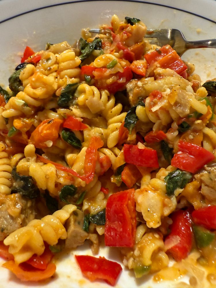 Red peppers orange tomatoes and hints of eggplants with lots of green basil on top of fusilli pasta.
