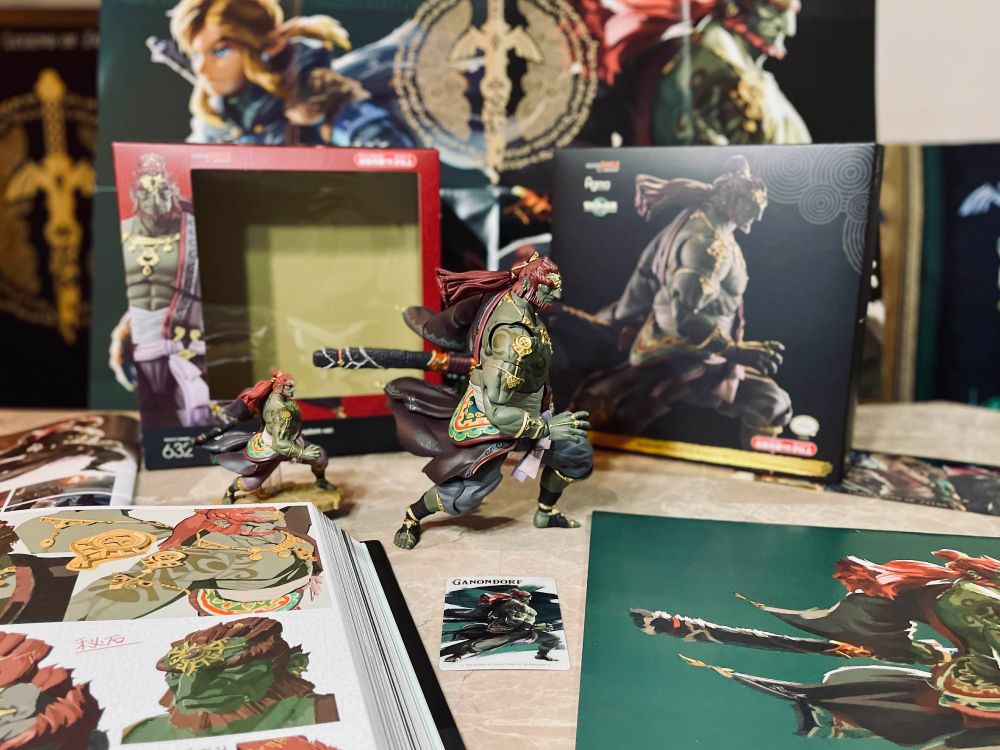 Ganondorf figma figure in the same pose as the TotK Ganondorf Amiibo, looking to the side in a "battle ready" pose, holding a sheathed Gloom Sword; box (front side); other TotK merch featuring Ganondorf