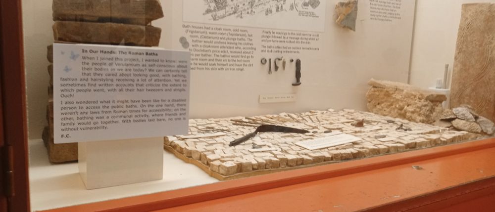 Label in a display case showing some Roman bath tiles. The label is written by a disabled person, and talks about physical access to the baths and body image in the Roman world.