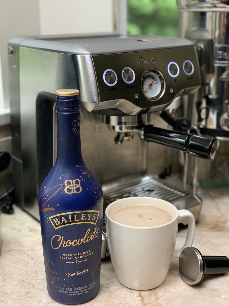 Photograph of a cappuccino maker with a large cup of coffee in front next to a bottle of Baileys chocolate liqueur 