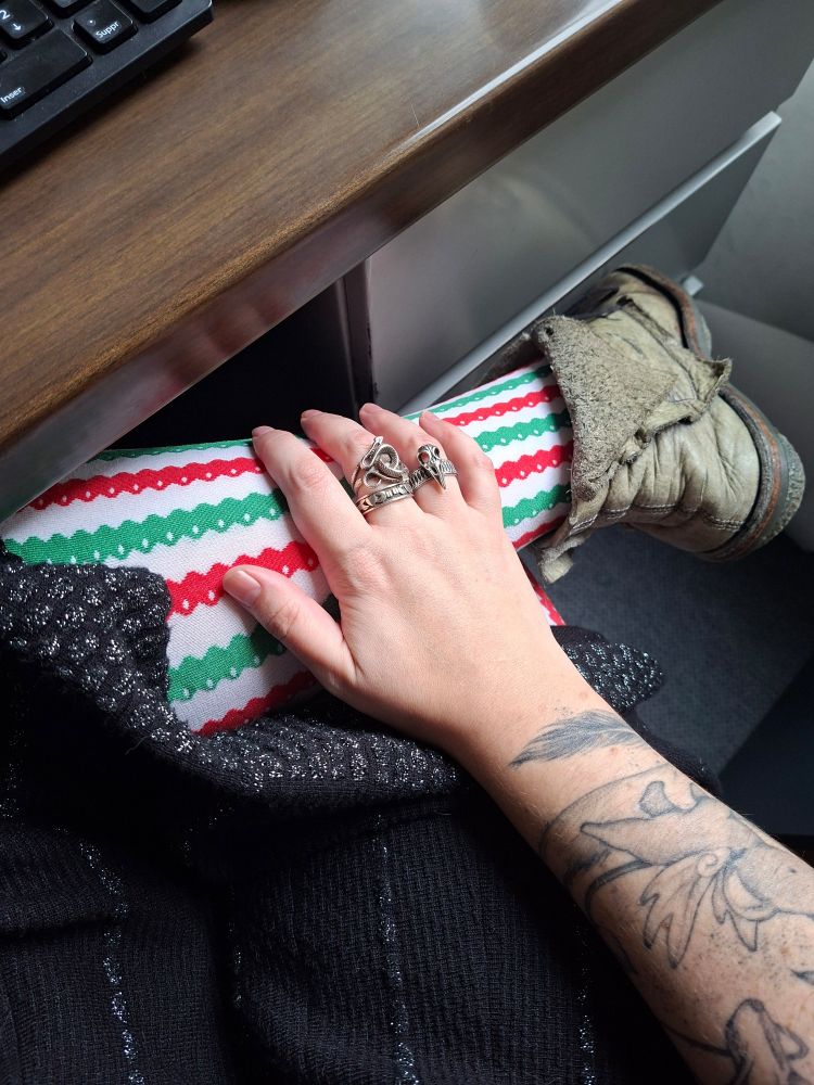 Photo prise a mon bureau. On y voit des collants rouge blanc et vert. Une robe noire et argent et ma main avec 3 bagues 