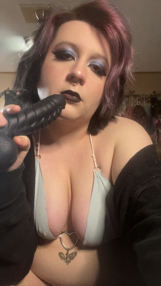 Onyx looking at the camera seductively and holding a dragon dildo in one hand. 