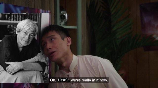 screenshot of Jason Mendoza from The Good Place in which a picture of Ursula K Le Guin has been shopped in. the text reads "Oh, Ursula, we're really in it now."