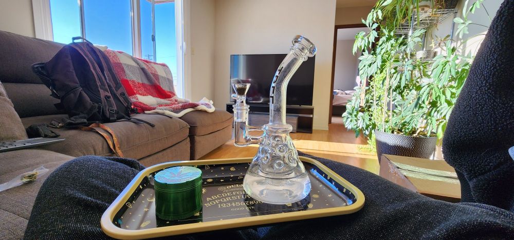 1st person pov. Sitting on couch in living room. Bong and grinder on a rolling tray. Lots of sun from balcony doors.