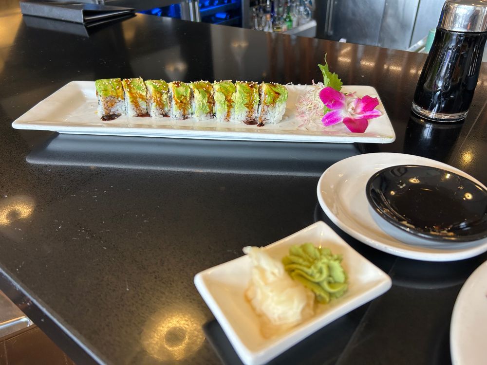 Hapa Caterpillar sushi roll, with freshwater eel and topped with avocado. Plate is garnished with a fresh orchid bloom and microplaned radish.