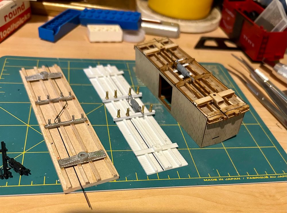 Photo of workbench showing 3 freight cars in various states of assembly. On left a customized Camino Models kit that will become a CRR of NJ 30000 series boxcar. It’s about to get brake gear. Center, an F&C kit of a Ma&Pa 700 series boxcar with new needle beams and queen posts. That’ll become a 500 series car. On right a BTS kit of a PRR XA boxcar, as updated with air brakes. It will become a Union Line boxcar. 