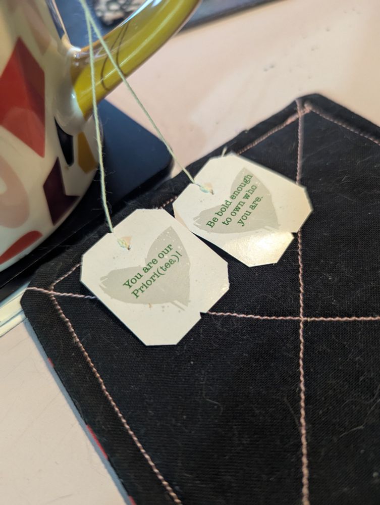 Good Earth tea bags in a multicolored cup. The tea bag tags have quotes on the them. Quote "You are our Priori(tea)!" And " Be bold enough to own who you are."