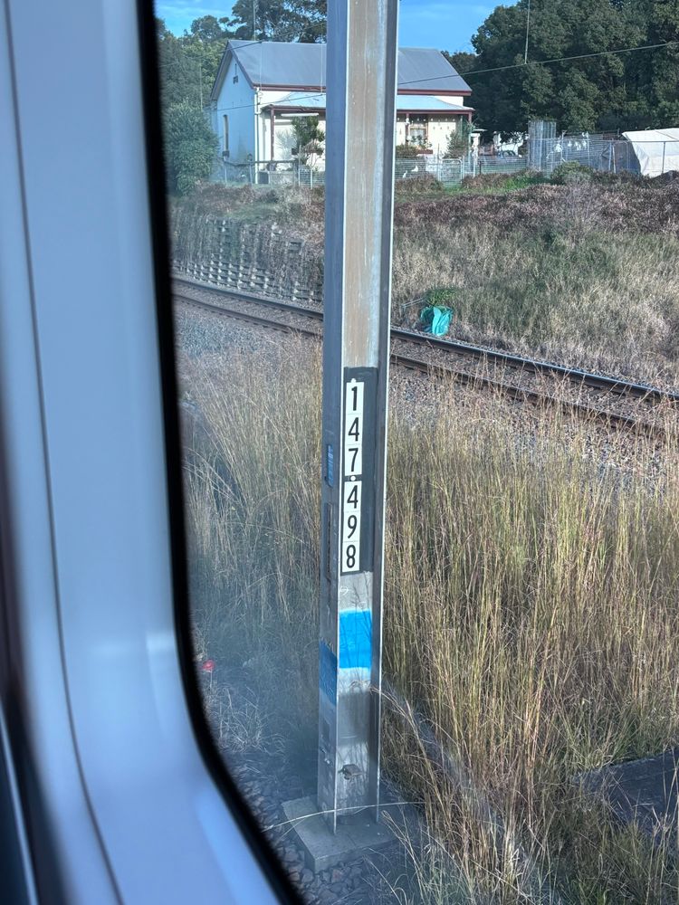 Distance marker on an electrified railway catenary pole reading “147.498” indicating the pole is 147.489km from Sydney Central. 